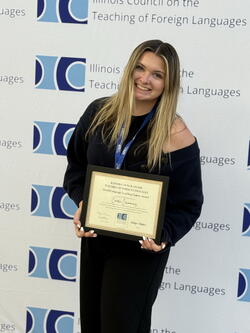 Caera Crimmins holding the award up in front of the ICTFL conference photo backdrop wall