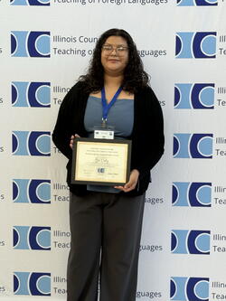 Itzel Ordaz holding the award up in front of the ICTFL conference photo backdrop wall
