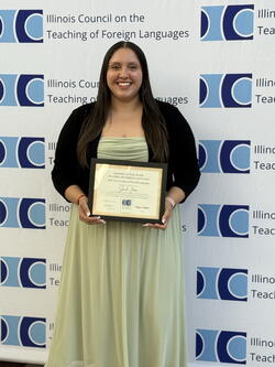 Sheila Jara holding the award up in front of the ICTFL picture backdrop wall